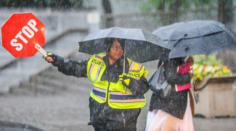 Atlanta police officer A. Bradley used her umbrella and stop sign to help cross City Hall workers across the street on Trinity Avenue in downtown Atlanta in the poring rain on Tuesday, April 15, 2015.