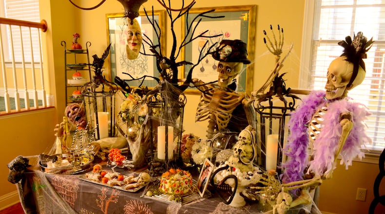 The mad scientist, in his top hat, and the bride in her boa, host a wicked wedding reception in the dining room. The skeleton hosts sit atop the serving table that is decorated with a trio of large black lanterns and baskets of spider-infested flowers. Aluminum serving pieces and mercury glass bottles add a glow and hint of glamour to an otherwise bare-bones display. Items from Pottery Barn, HomeGoods and Grandin Road.