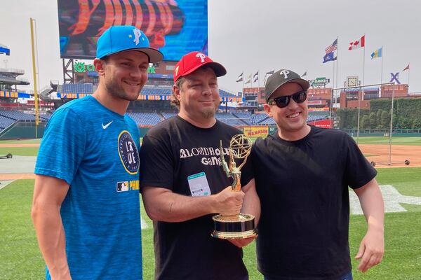 Philadelphia Phillies shortstop Trea Turner, left, poses with Phillies fan Jon McCann, center, and documentary producer Kyle Thrash with a sports Emmy won for best sports documentary "The Turnaround", the story how McCann inspired a city-wide movement to cheer for instead of boo for Turner, before a baseball game against the Toronto Blue, Jays, Friday, June 13 , 2025, in Philadelphia (AP Photo/Dan Gelston)