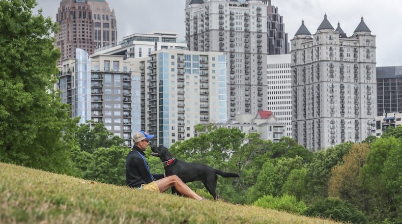 Ron Hoffman sits in Piedmont Park in Midtown with his black labrador retriever, Georgia, on April 14. The above average temperatures Georgia has felt so far this year may continue into summer, a new federal forecast shows. (John Spink / John.Spink@ajc.com)