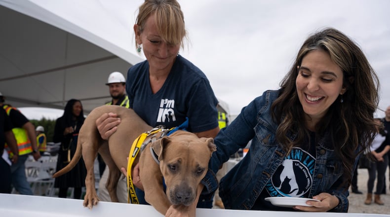 Lifeline Animal Project's representative dog, Brandy, supported by Fulton County Animal Services Director of Operations Belinda Bell (left) and Lifeline Chief Marketing Officer Heather Friedman (right) , stamps her paw on the inaugural beam that will be built into the new shelter in Fulton County, on Friday, May 19, 2023. (Olivia Bowdoin for the Atlanta Journal Constitution).