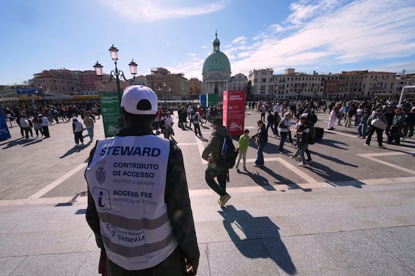 Stewards check tourists' QR codes outside the main train station in Venice, Italy, Friday, April 18, 2025, as the city for a second year is charging day-trippers an arrivals tax. (AP Photo/Antonio Calanni)