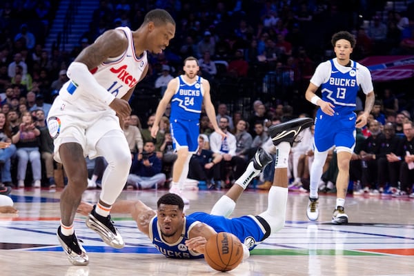 Milwaukee Bucks' Giannis Antetokounmpo, center, dives for the loose ball with Philadelphia 76ers' Lonnie Walker IV, left, looking on during the first half of an NBA basketball game, Thursday, April 3, 2025, in Philadelphia. (AP Photo/Chris Szagola)