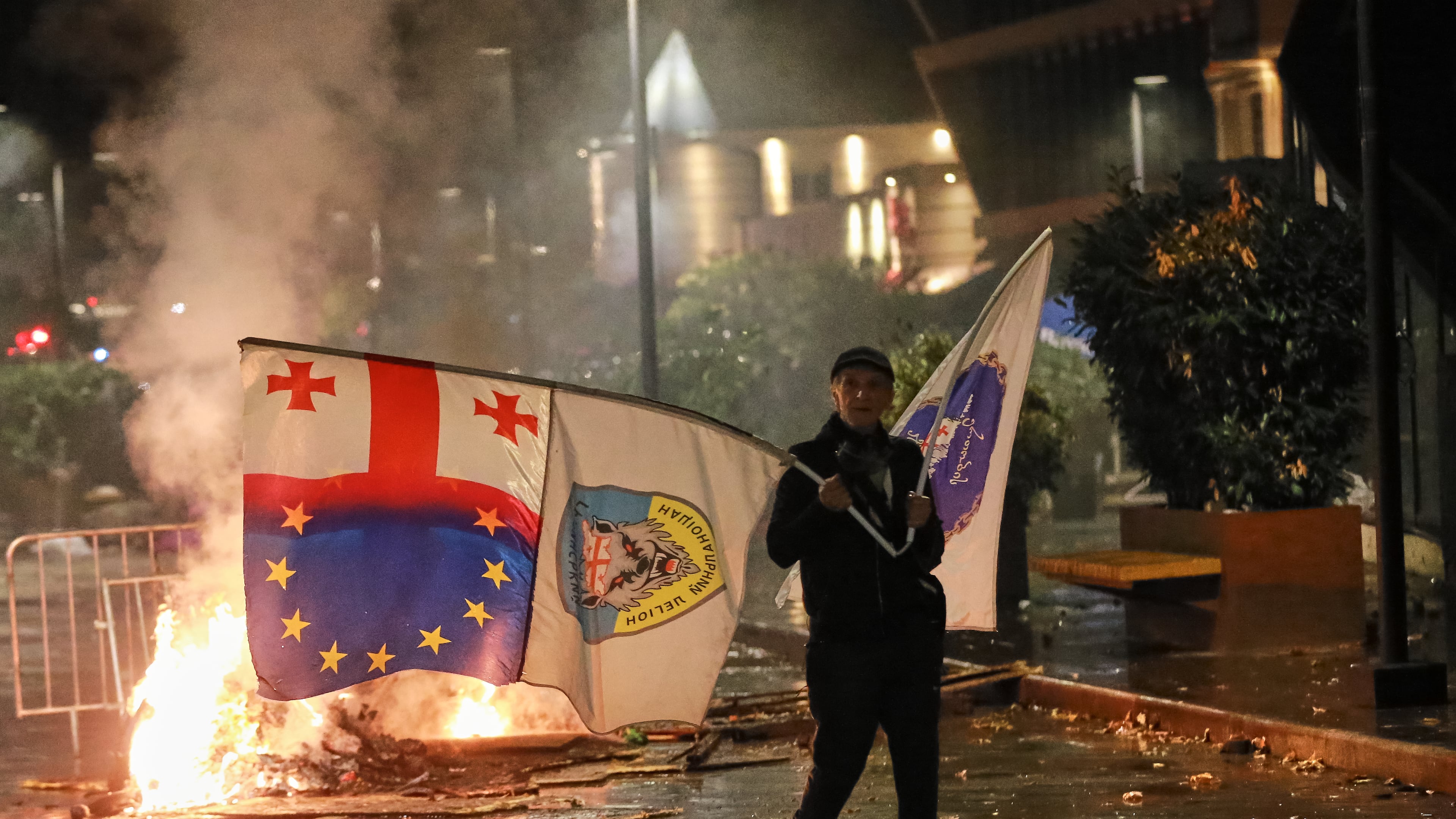 A demonstrator with a Georgian national, EU and other flags walks in front of police line during an opposition rally in the city center of Tbilisi, Georgia, on Saturday, Oct. 4, 2025, boycotting the municipal elections and calling for the release of political opponents. (AP Photo/Zurab Tsertsvadze)