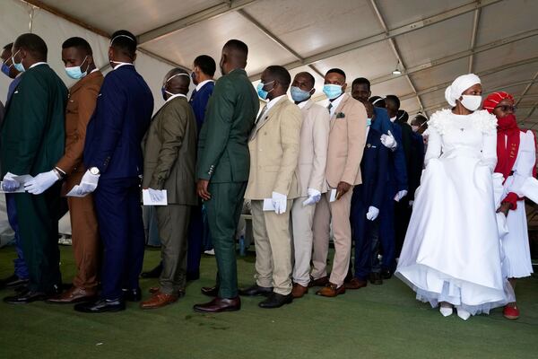Groomsmen queue to collect their partner's flower bouquet inside a marquee ahead of the mass Easter weddings for 3,000 people, some polygamous, at the International Pentecost Holiness Church in Heidelberg, east of Johannesburg, South Africa, Sunday, April 20, 2025. (AP Photo/Themba Hadebe)