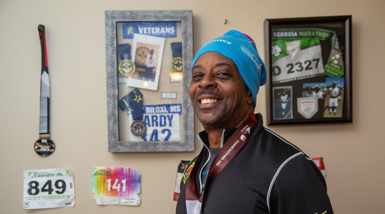 Eugene Hardy Jr. stands with some of the running medals he has won recently in his apartment in Stone Mountain. He was a combat veteran, was formerly homeless, jobless and battling addition. He camped out in the woods near high school stadiums so he could run around the track and focus on getting his life back in order. Two VA programs are now helping him with a home and a job. (Photo by Phil Skinner)