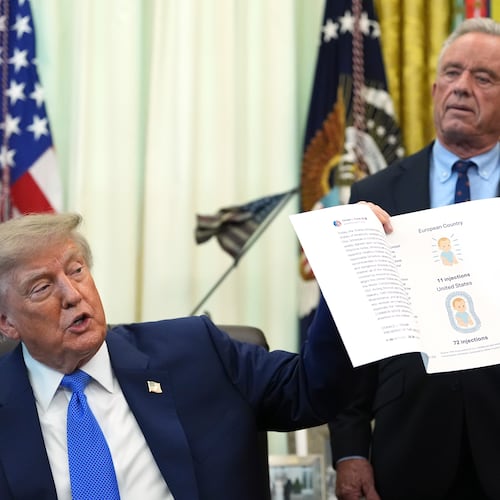 President Donald Trump holds up an image taken from his Truth Social account as Health and Human Services Secretary Robert F. Kennedy Jr. watches during a meeting to sign an executive order about vaccines, Monday, Aug. 10, 2026, in the Oval Office of the White House in Washington. (AP Photo/Jacquelyn Martin)