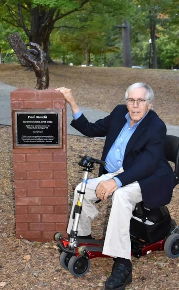 Paul Bianchi poses with a statue dedicated to him on the campus of The Paideia School. The statue of a hand holding an eraser refers to Bianchi's annual tradition of throwing an eraser into a crowd of children each school year, with the kid catching the eraser destined to be a teacher. (Courtesy of the Paideia School)