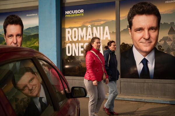Women walk by posters of Nicusor Dan, the mayor of Bucharest and presidential candidate in the upcoming May elections in Bucharest, Romania, Friday, March 28, 2025. (AP Photo/Vadim Ghirda)