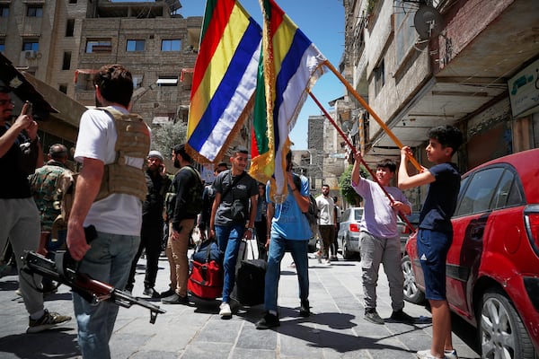 Druze boys hold their sect religious flags stand next to Druze gunmen, a day after clashes between members of the minority Druze sect and pro-government fighters left at least four people dead in the southern suburb of Jaramana, Damascus, Syria, Tuesday, April 29, 2025. (AP Photo/Omar Sanadiki)