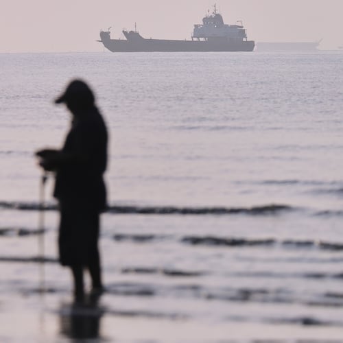 Cargo ships and service vessels are anchored in the Strait of Hormuz, as a person stands in shallow water, off Bandar Abbas, Iran, Sunday, May 31, 2026. (Amirhosein Khorgooi/ISNA via AP)