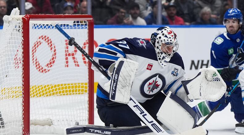 Winnipeg Jets goalie Connor Hellebuyck (37) makes a save with the shaft of his stick during the third period of an NHL hockey game against the Vancouver Canucks, in Vancouver, on Tuesday, Nov. 11, 2025. (Darryl Dyck/The Canadian Press via AP)