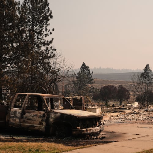 A burned truck sits in a driveway near several destroyed homes in a residential neighborhood Tuesday, Aug. 4, 2026, after a wildfire hit the northern part of Spokane, Wash. (AP Photo/Lindsey Wasson)