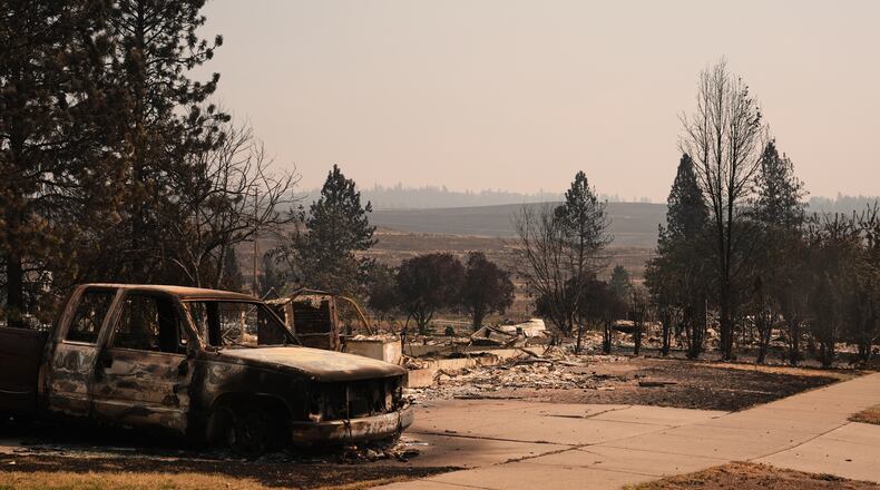A burned truck sits in a driveway near several destroyed homes in a residential neighborhood Tuesday, Aug. 4, 2026, after a wildfire hit the northern part of Spokane, Wash. (AP Photo/Lindsey Wasson)