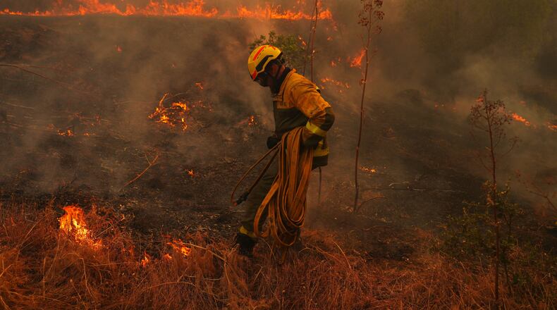 A firefighter carries a hose while battling a wildfire in San Martin de Valdeiglesias, west of Madrid, Spain, Sunday, July 26, 2026. (AP Photo/Manu Fernandez)