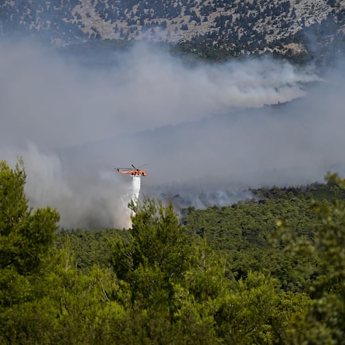 A firefighting helicopter drops water over a smoke-filled forest during a wildfire near Porto Germeno, northwest of Athens, Greece, Sunday, Aug. 2, 2026. (AP Photo/Michael Varaklas)