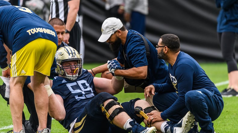 Former Georgia Tech offensive lineman Scott Morgan is treated at an April 2019 practice by head football athletic trainer Mark Smith (hat), assistant football athletic trainer Eric Avila (behind Morgan) and physician Edward Jackson. (Danny Karnik/Georgia Tech Athletics)