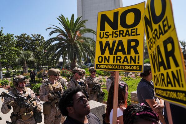 Anti-war demonstrators hold up signs as U.S. Marines guard the Wilshire Federal Building in Los Angeles, Sunday, June 22, 2025. (AP Photo/Jae C. Hong)