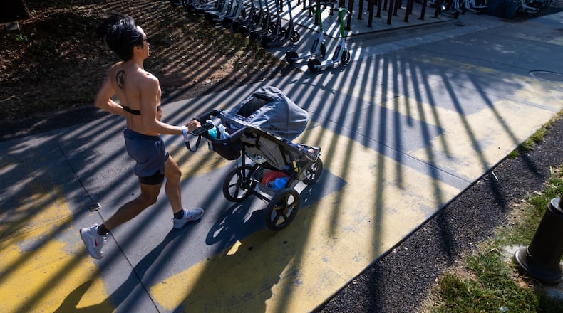 Dow Lin pushes his 14-month old son in the shadows of the Steel Columns Sculpture on the Beltline Eastside Trail at Angier Springs Road on a mild Tuesday, Sept. 10, 2024. (John Spink/AJC)