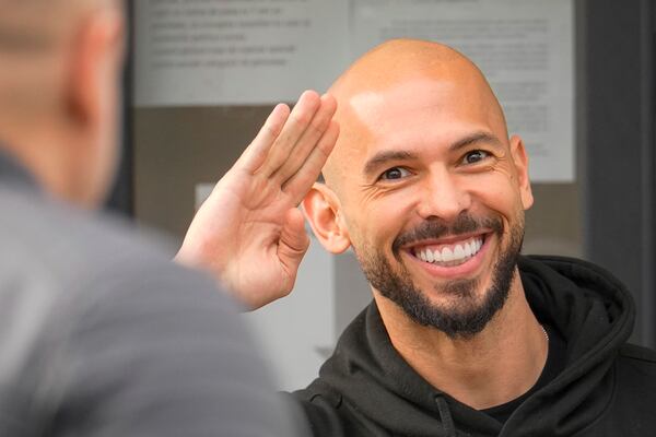 Andrew Tate waves as he checks in at a police station as part of his judicial control, which requires him to appear before judicial authorities in Romania when summoned, after returning from the United States, in Voluntari, Romania, Monday, March 24, 2025. (AP Photo/Vadim Ghirda)
