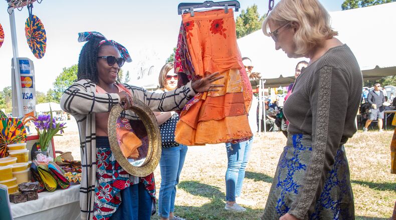 Rejoyce Dablah (R) helps a customer pick out one of her dresses from Ghana during the Johns Creek International Festival on October 23, 2021. STEVE SCHAEFER FOR THE ATLANTA JOURNAL-CONSTITUTION