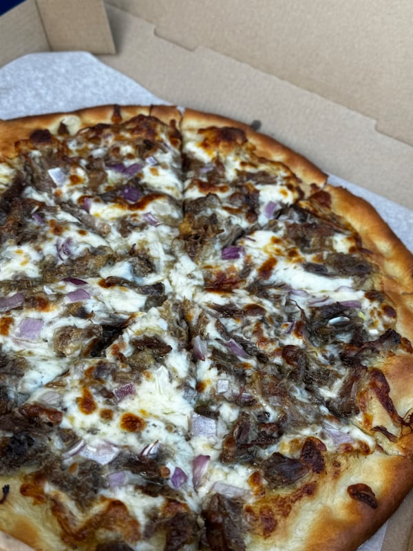 A large pizza in a box with heavily applied toppings including shredded oxtail and melted white cheese