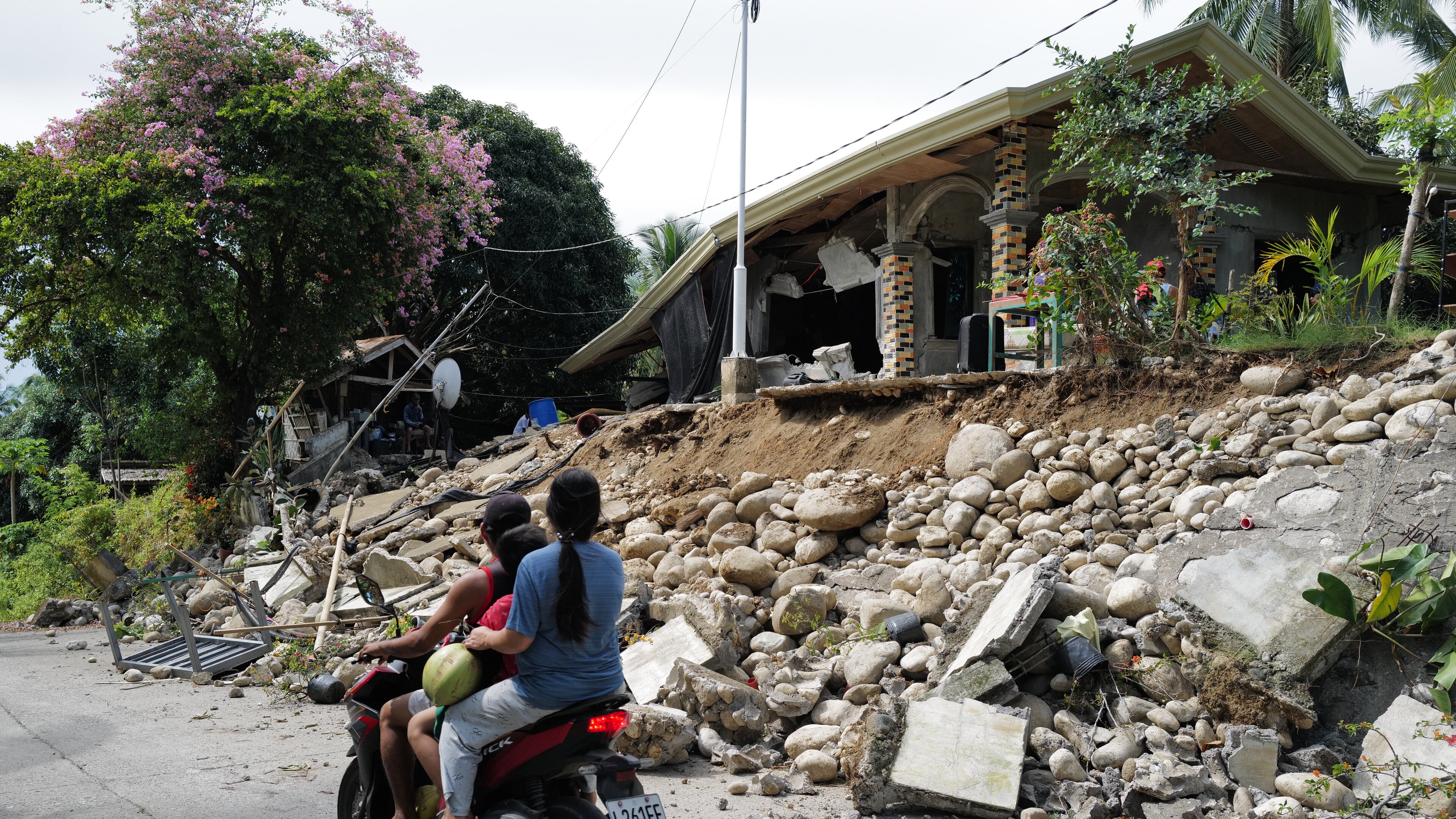 Motorists move past a house that was damaged by a strong earthquake in Manay town, Davao Oriental province, southern Philippines Saturday, Oct. 11, 2025. (AP Photo/Jeoffrey Maitem)