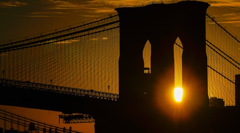 FILE - The sun rises behind the Brooklyn Bridge on Oct. 11, 2023, in New York. (AP Photo/Kiichiro Sato, File)