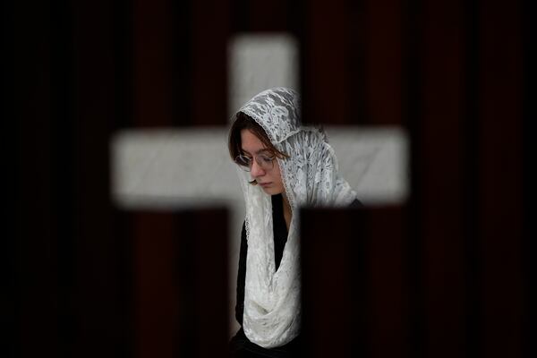 Photographed through an opening in the shape of a cross, a person prays during Mass in honor of Pope Francis, following the Vatican's announcement of his death, at the Cathedral in Brasilia, Brazil, Monday, April 21, 2025. (AP Photo/Eraldo Peres)