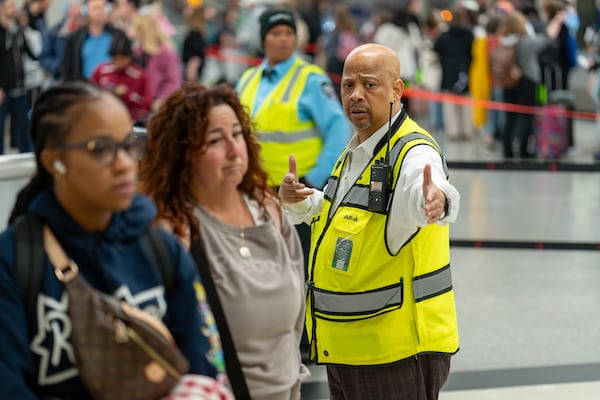 An Atlanta airport worker directs morning travelers to the main checkpoint at Hartsfield-Jackson Atlanta International Airport on Thursday morning. (Ben Hendren for the AJC)