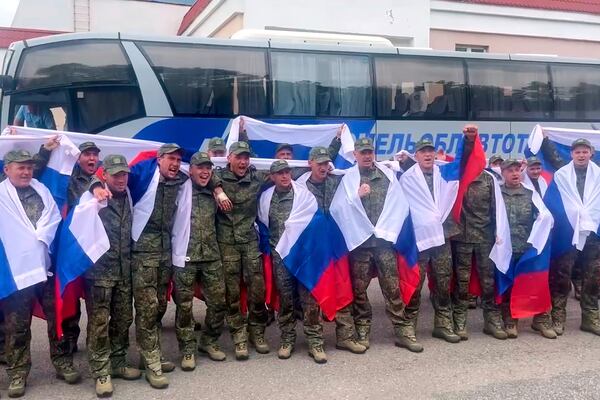 In this photo taken from video distributed by Russian Defense Ministry Press Service on Thursday, June 19, 2025, Russian servicemen with Russian national flags pose for a photo at an exchange area in Belarus after returning from captivity during a POWs exchange of a group of servicemen between Russia and Ukraine. (Russian Defense Ministry Press Service via AP)