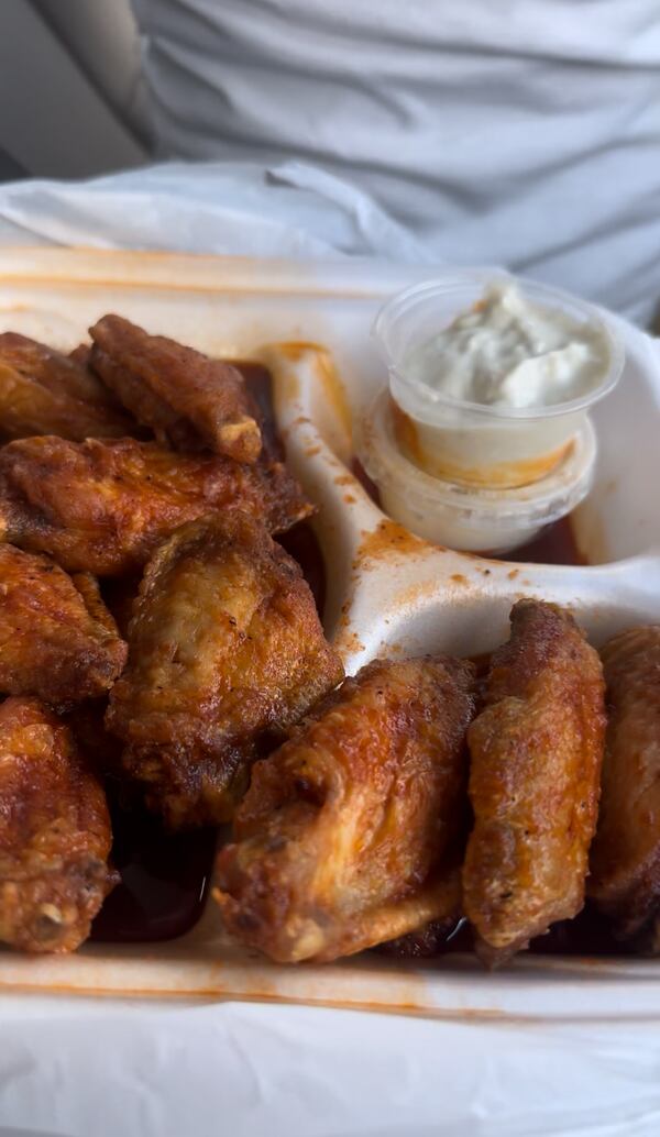 A segmented takeout box filled with hot wings and an open side dish of blue cheese.