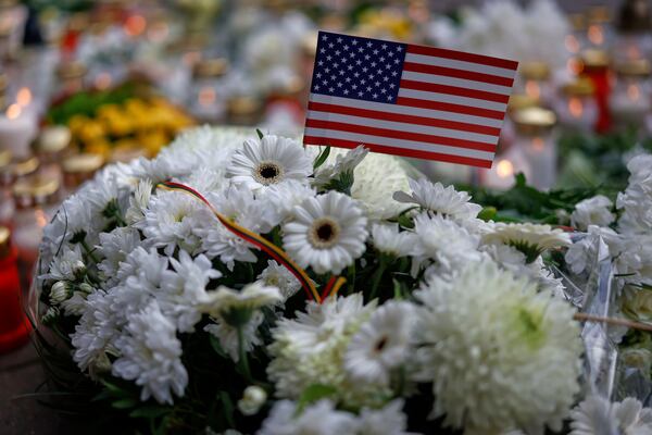 A U.S. national flag and flowers in memory of three soldiers found dead on Monday at a training range in Pabrade, are on the ground near the U.S. Embassy in Vilnius, Lithuania, Tuesday, April 1, 2025. (AP Photo/Mindaugas Kulbis)