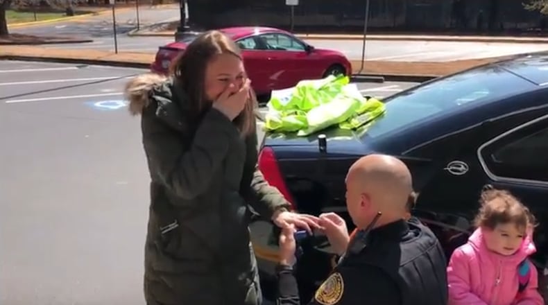 Officer Matthew Jay (kneeling) proposes to Aliza Sandler. Jay was at Weinstein School at the Marcus Jewish Community Center of Atlanta in Dunwoody, where Sandler works as a teacher, for "Community Helpers Week."