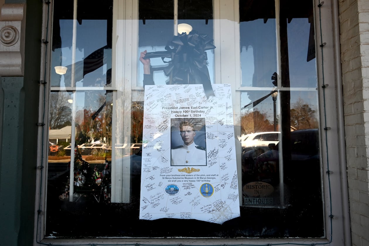 Tim Buchanan (hand), manager of the Buffalo Cafe, decorates a portrait of former President Jimmy Carter with a black ribbon, in downtown Plains, Wednesday, January 8, 2025. (Hyosub Shin / AJC)