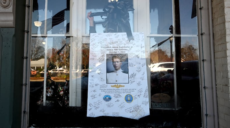 Tim Buchanan (hand), manager of the Buffalo Cafe, decorates a portrait of former President Jimmy Carter with a black ribbon, in downtown Plains, Wednesday, January 8, 2025. (Hyosub Shin / AJC)