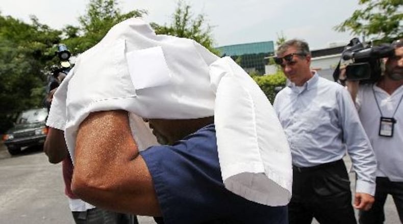 A doctor covers his head as he leaves during a ” pill mill” raid near Tucker in 2012. More than a half dozen patients were taken away in cuffs to a prisoner transport van. The doctors and employees were allowed to leave following the raid. The owner of the business was also removed in cuffs and taken away in a prisoner transport van. CURTIS COMPTON / CCOMPTON@AJC.COM AJC File Photo