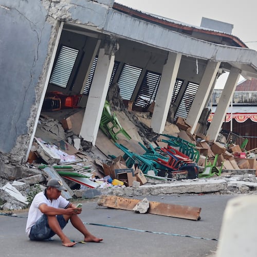 A man checks his phone near a building collapsed due to an earthquake, in Reok, East Nusa Tenggara province, Indonesia, Sunday, Aug. 16, 2026. (AP Photo/Aquila Handayani Abbas)