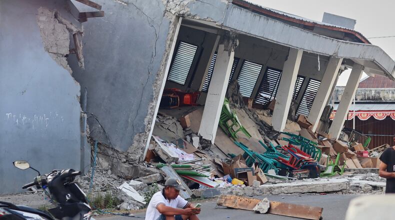 A man checks his phone near a building collapsed due to an earthquake, in Reok, East Nusa Tenggara province, Indonesia, Sunday, Aug. 16, 2026. (AP Photo/Aquila Handayani Abbas)