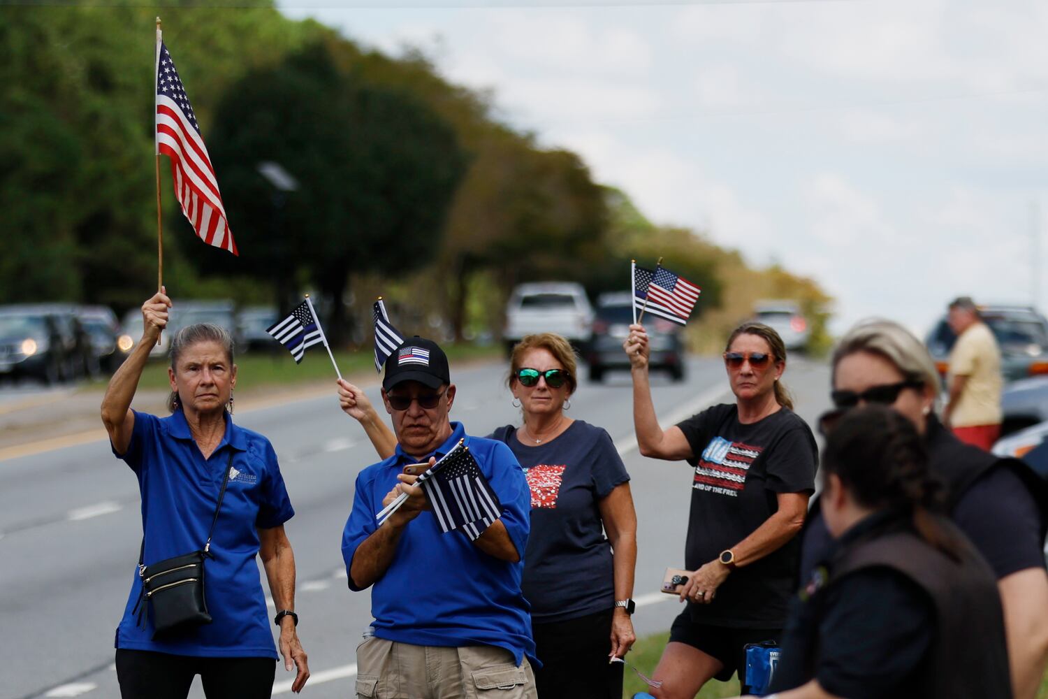 People stand by Dallas Highway holding U.S. flags to pay respect to Marshall Samual Ervin Jr during the procession over Dallas Highway on Thursday, September 15, 2022. Miguel Martinez / miguel.martinezjimenez@ajc.com 