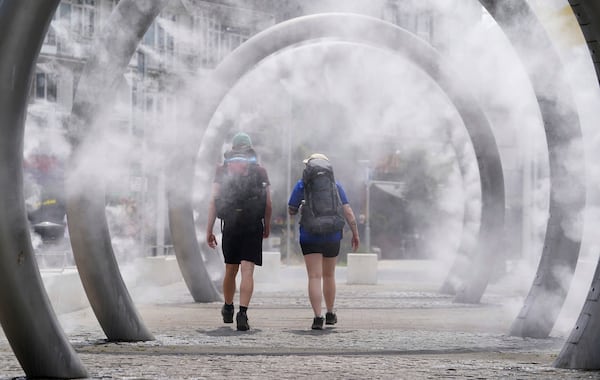 Walkers cool off as they walk through a water feature spraying a fine mist in Dover, England, Friday, June 20, 2025. (Gareth Fuller/PA via AP)