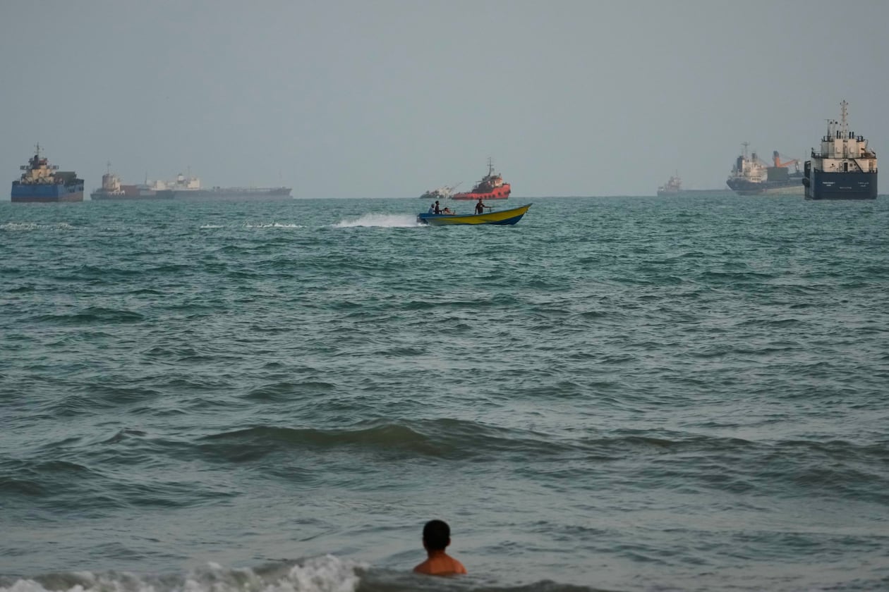 A swimmer remains near the shore as a motorboat passes commercial vessels anchored in the Strait of Hormuz off Bandar Abbas, Iran, Friday, Sept. 4, 2026. (AP Photo/Vahid Salemi)