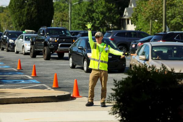 A volunteer directs traffic as automobiles lineup to receive food during the weekly drive-up food pantry at First Presbyterian Church in Marietta. (Jason Getz/AJC)