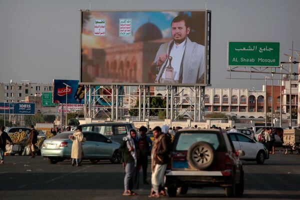 Yemenis stand under a street billboard displaying a picture of Abdul Malik al-Houthi, the leader of the Houthi movement, in Sanaa, Yemen, Tuesday, March 18, 2025. (AP Photo/Osamah Abdulrahman)