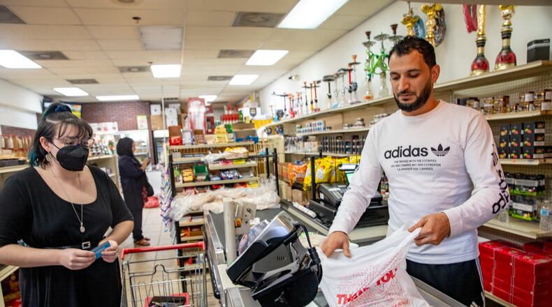 New American Pathway staff China Myrick, left, check out with Raghb Moshaal, right, at Al-Salam International Groceries in Clarkston Monday, November 22, 2021 as they prepare for an Afghan family of five, with one on the way, to arrive and relocate to the community. The family of two adults and three small children will need to make the food last two weeks and the organization is also preparing an apartment for the refugee family. (Jenni Girtman for The Atlanta Journal-Constitution)