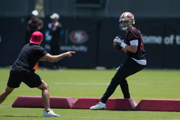 San Francisco 49ers quarterbacks coach Mick Lombardi, left, gestures as quarterback Mac Jones runs a drill during NFL football practice Wednesday, June 4, 2025, in Santa Clara, Calif. (AP Photo/Jeff Chiu)