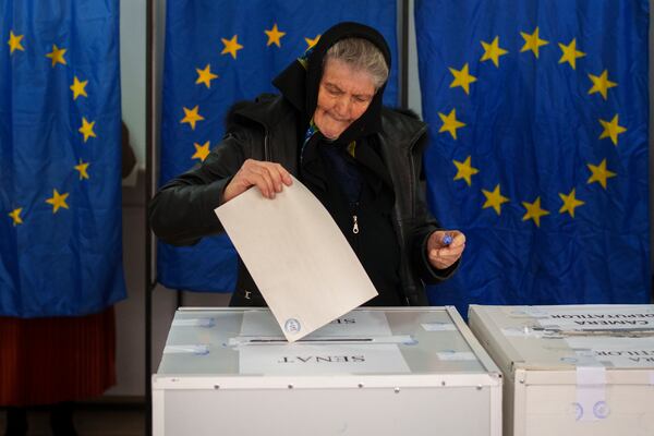 FILE - A woman casts her vote in a station with European Union flags as curtains for the cabins, in the country's parliamentary elections, in Baleni, Romania, Dec. 1, 2024. (AP Photo/Vadim Ghirda, File)