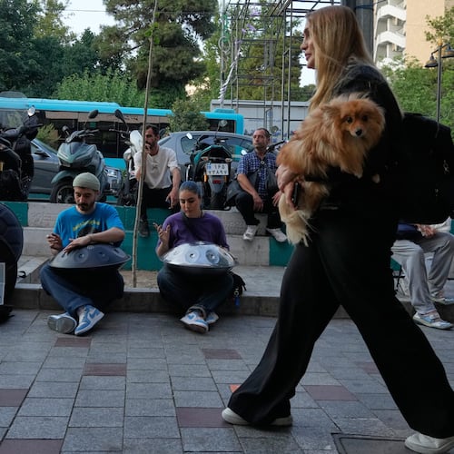 Street musicians play music as a woman carries a dog on a sidewalk in northern Tehran, Wednesday, June 10, 2026. (AP Photo/Vahid Salemi)
