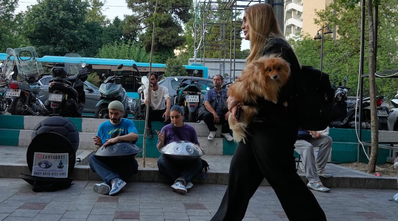 Street musicians play music as a woman carries a dog on a sidewalk in northern Tehran, Wednesday, June 10, 2026. (AP Photo/Vahid Salemi)
