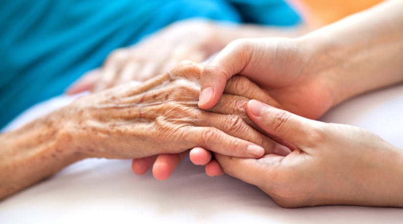 Woman holding senior woman's hand on hospital bed (stock photo).